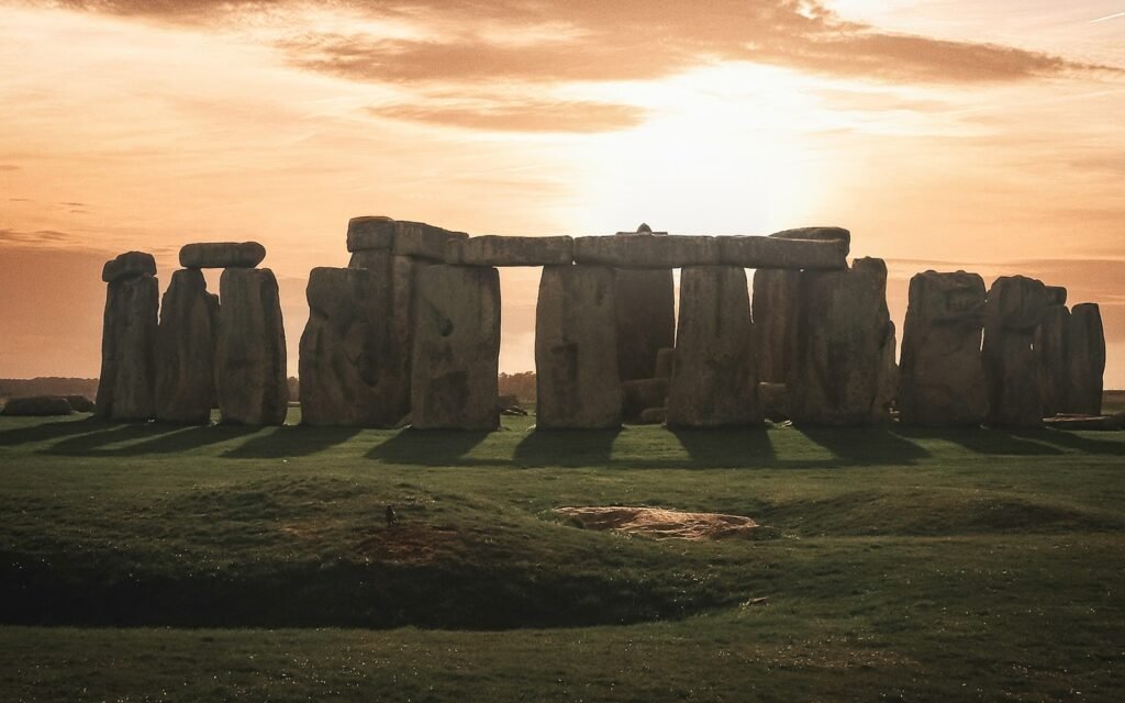 a stonehenge in a field with the sun setting behind it